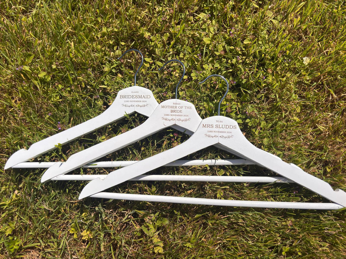 Close-up of three white wedding hangers engraved with bridal party names, roles and wedding date.