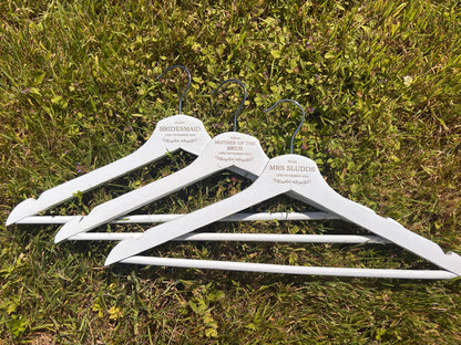 Close-up of three white wedding hangers engraved with bridal party names, roles and wedding date.
