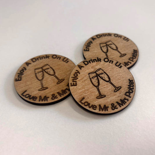 Personalised round wooden wedding drink tokens engraved with champagne glasses and the couple's married names.