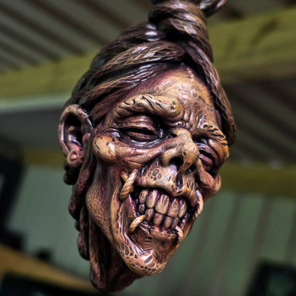 Close-up of a resin shrunken head showing prominent teeth, textured skin and grotesque facial wrinkles.