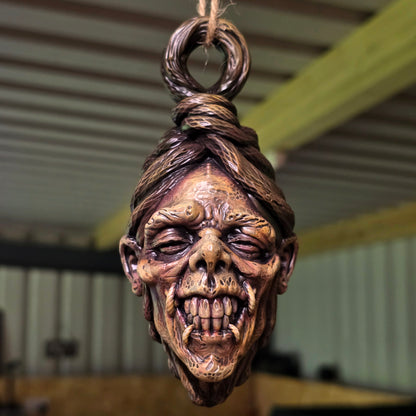 Front view of a hanging shrunken head sculpture with bared teeth, sunken eyes and twisted facial features.