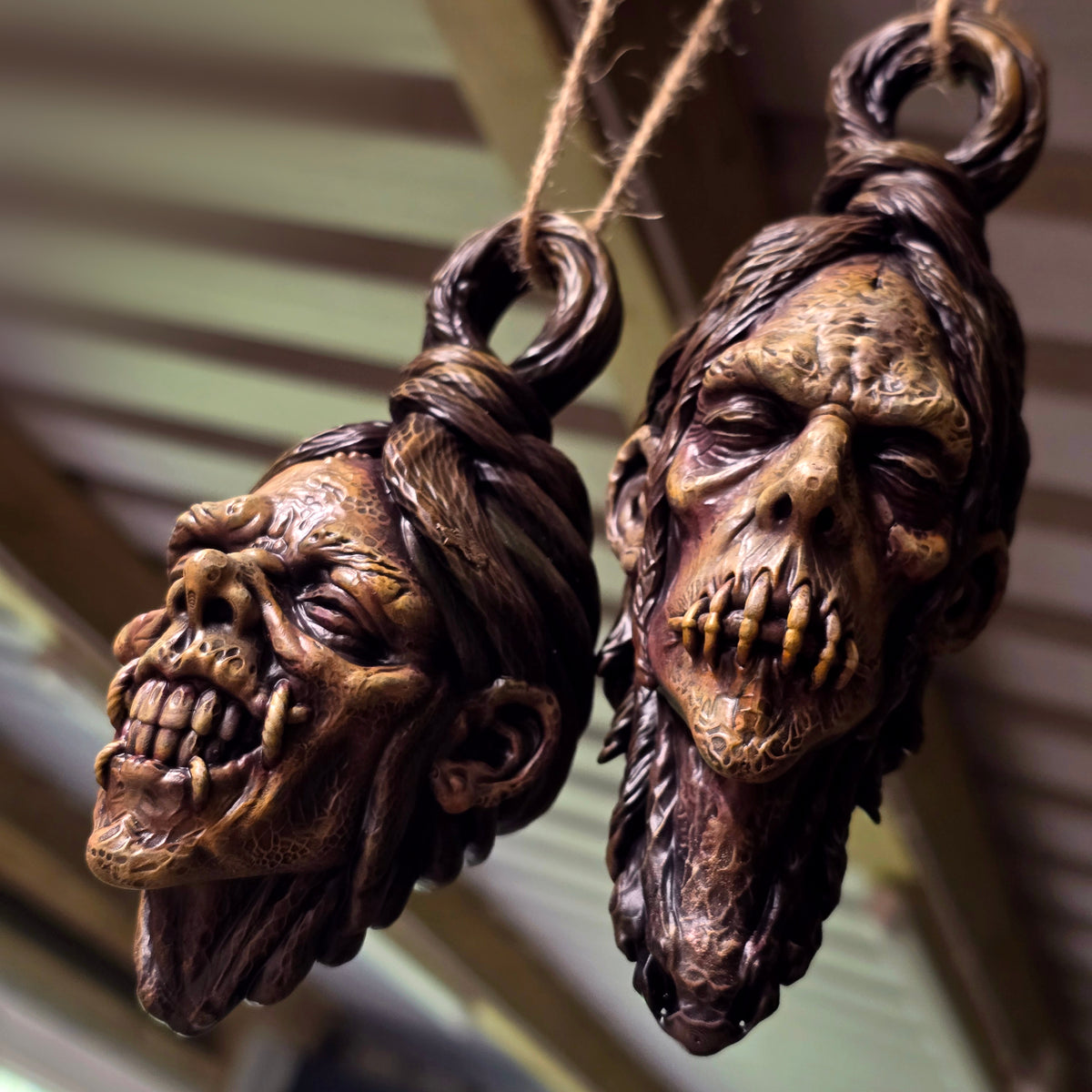Two hand-painted hanging shrunken head sculptures featuring exposed teeth and a stitched mouth.