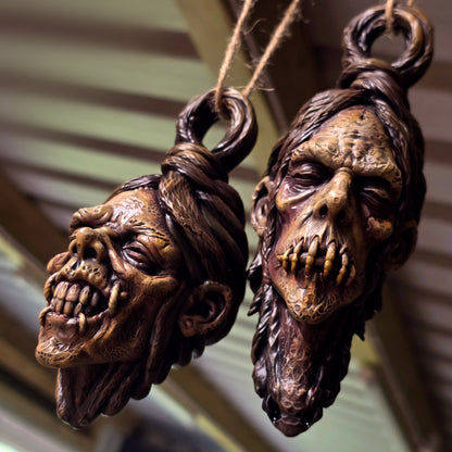Two hand-painted hanging shrunken head sculptures featuring exposed teeth and a stitched mouth.