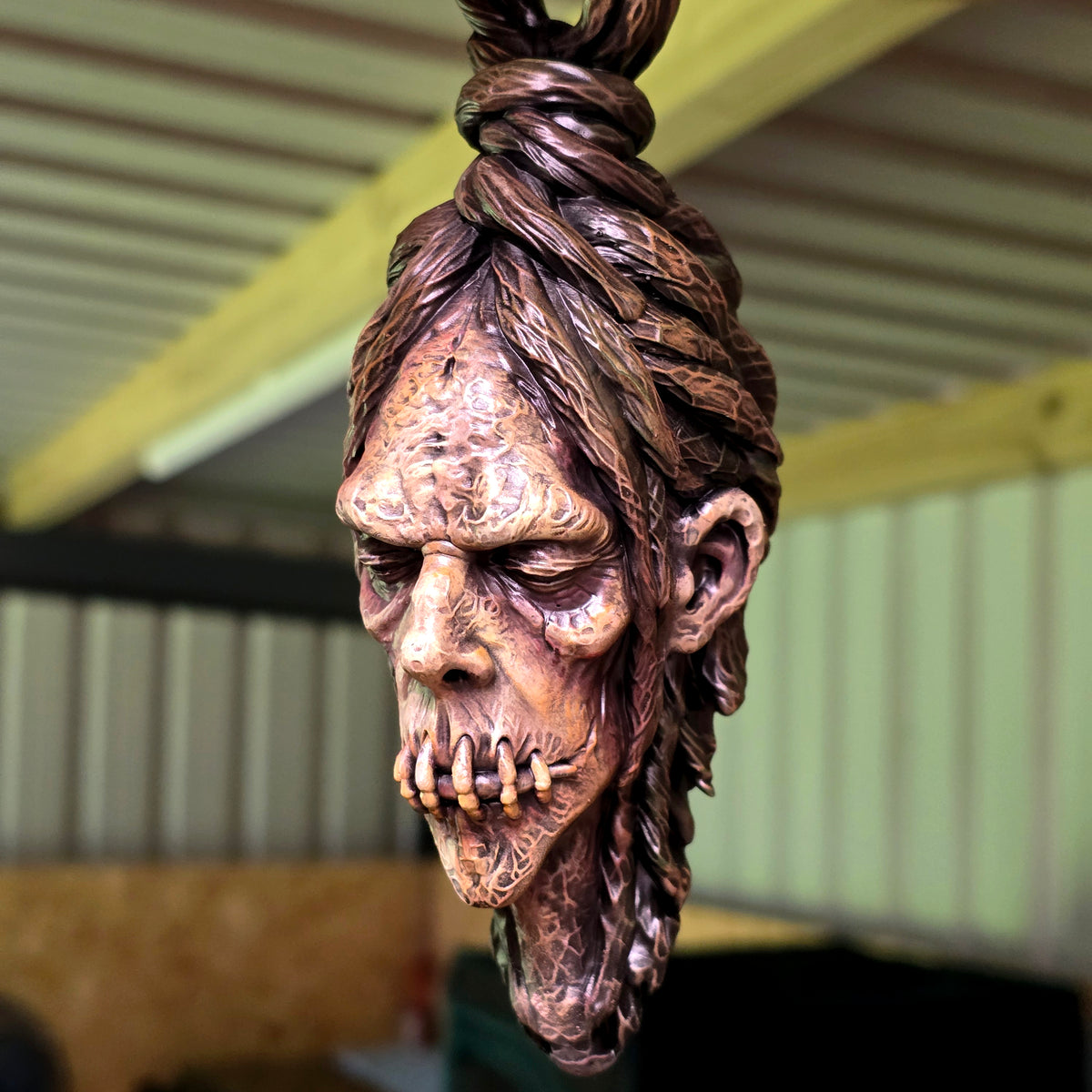 Three-quarter view of a hand-painted hanging shrunken head ornament with tightly stitched mouth.