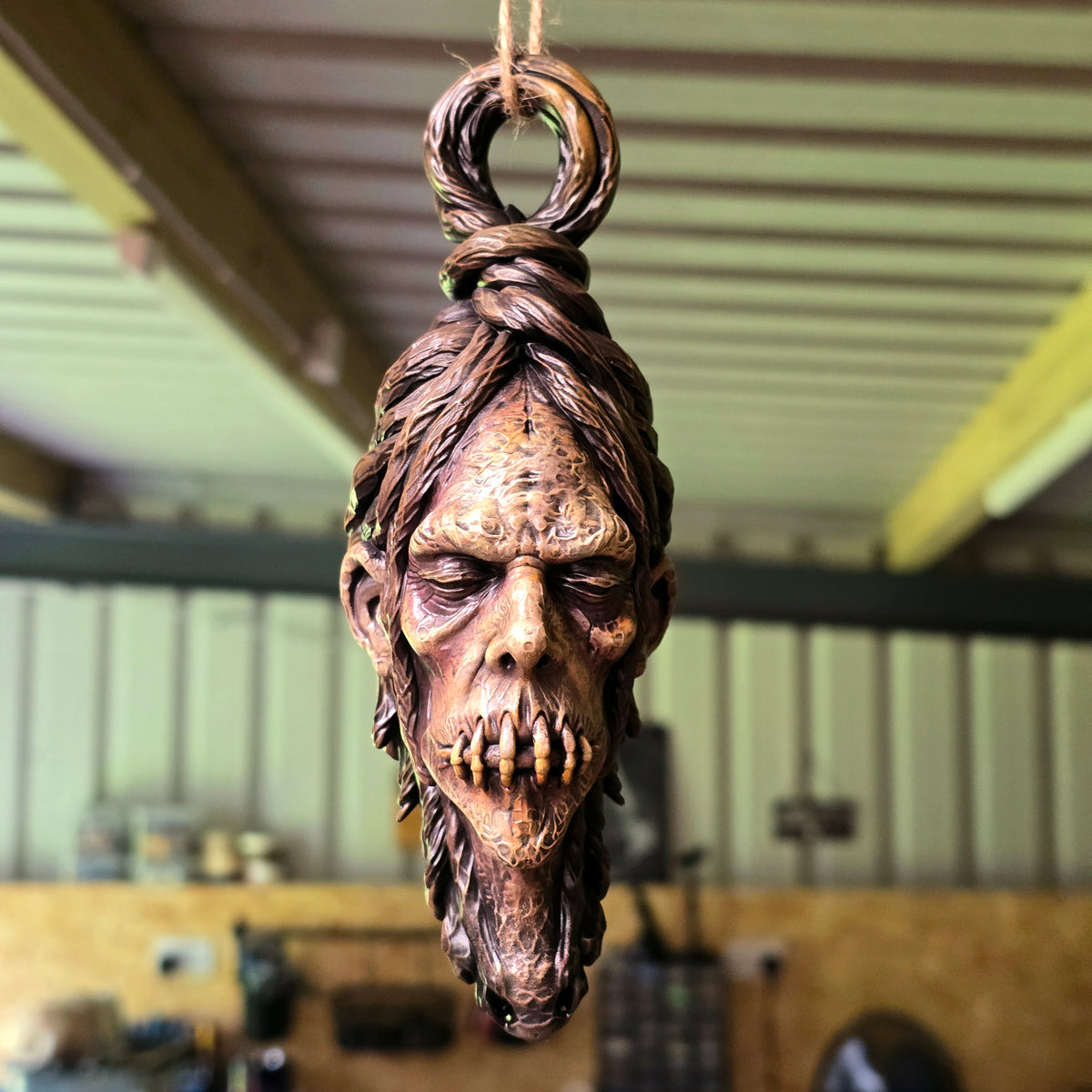 Front view of a resin shrunken head decoration with stitched lips, heavy eyelids and elongated features.