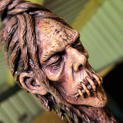 Angled view of a stitched-mouth shrunken head showing detailed wrinkles, sculpted hair and weathered skin.