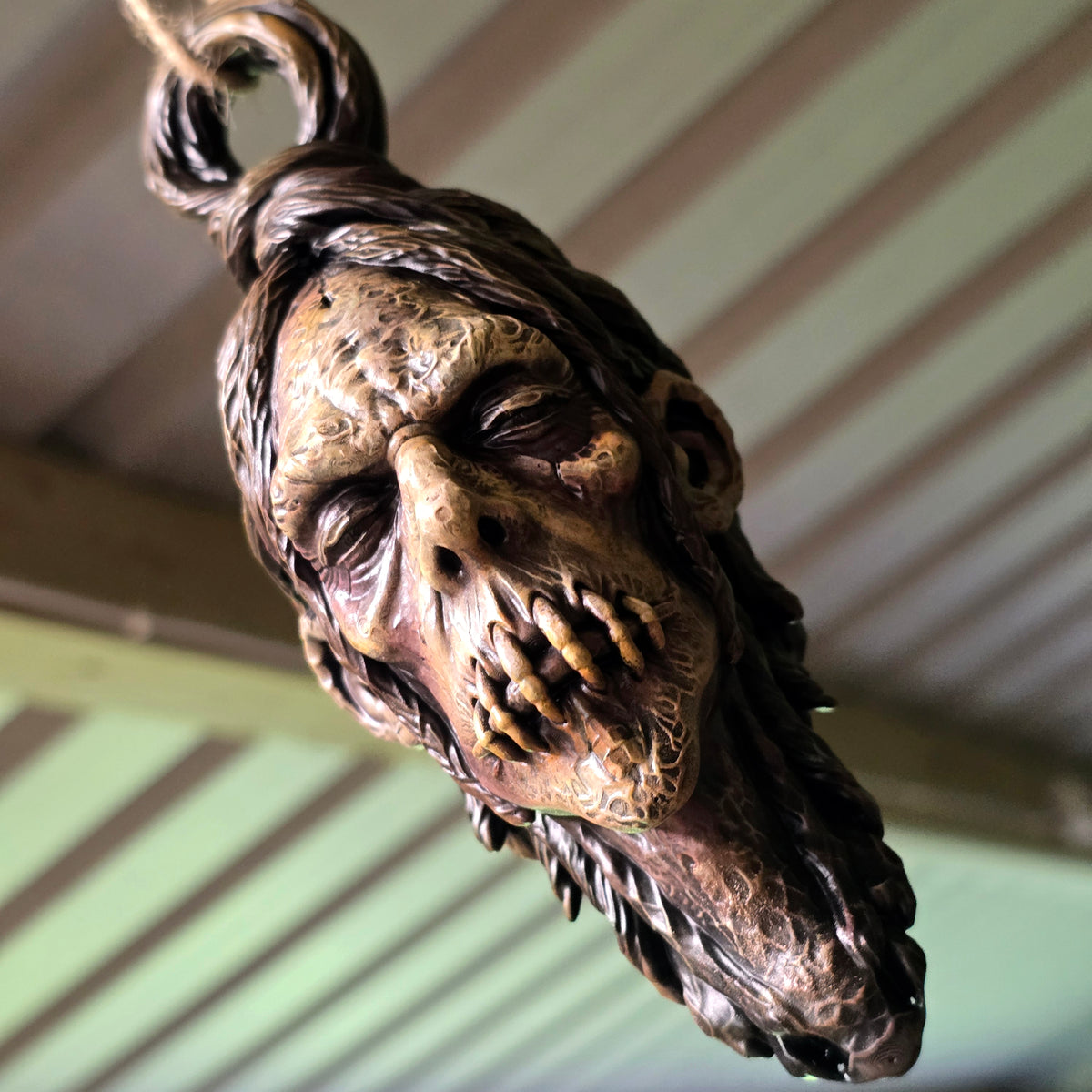 Low-angle close-up of a hanging shrunken head highlighting its stitched mouth and aged surface detailing.